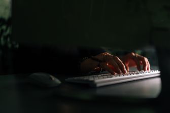 Close-up of hands typing on a computer keyboard in a dimly lit setting.