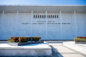 Exterior view of the Kennedy Center for the Performing Arts showing a white stone façade with a long engraved inscription along the wall.