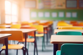 Bright empty classroom with colorful desks and chairs arranged in rows.