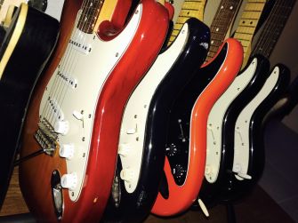 A row of Stratocaster-style electric guitars in various colors lined up on a display rack.
