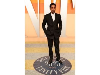 Man in a black suit posing on a circular platform at a formal event against an orange backdrop.
