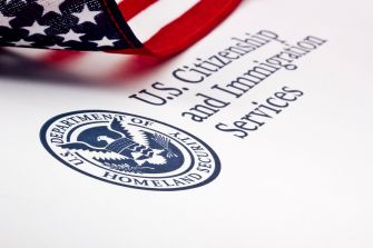 Close-up of a U.S. flag over a document bearing the Department of Homeland Security seal and the words U.S. Citizenship and Immigration Services.