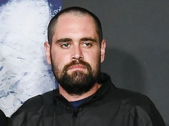 Portrait of a man with a short beard and dark hair wearing a dark jacket, looking to the left with a serious expression.