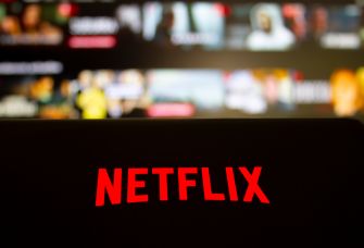 Red Netflix logo on a dark screen with a blurred streaming interface in the background.
