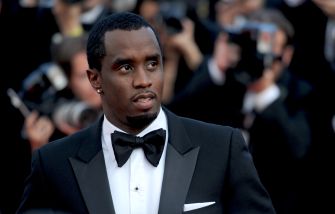 Man in a black tuxedo and bow tie on a red carpet, looking to the left.