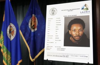 Mugshot-style portrait of a man displayed on an information board with flags in the background.