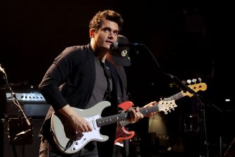 Male musician performing live on stage with a white electric guitar.