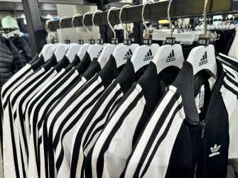 Adidas jerseys on hangers in a store display, prominently featuring the black-and-white three-stripe design.
