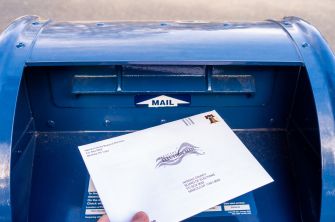 Blue curbside mailbox with a hand dropping a white envelope into the mail slot.