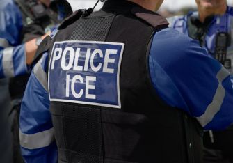 Officers in blue uniforms wearing protective vests labeled POLICE ICE.