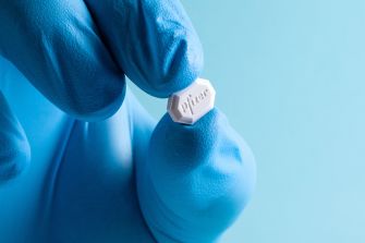 Close-up of a blue-gloved hand holding a small white tablet labeled Pfizer