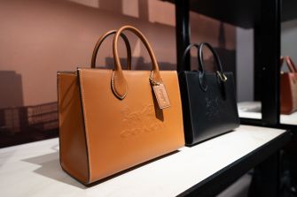 Tan and black leather handbags on a store display featuring Coach branding.