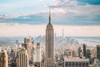 The Empire State Building rises above Manhattan’s skyline during daytime with a partly cloudy sky.