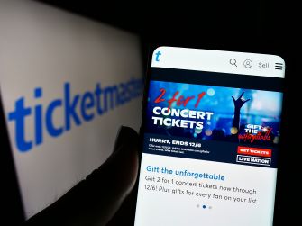 Close-up of a smartphone displaying Ticketmaster's site with a "2 for 1 CONCERT TICKETS" banner and a blurred Ticketmaster logo in the background.