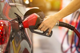 Close-up of a hand holding a red gas pump nozzle at a fueling station.