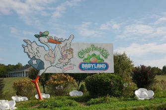 Outdoor Cabbage Patch Kids sign at Babyland General Hospital, featuring cartoon dolls and a bright blue sky.