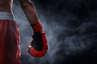 Close-up of a boxer’s red glove and red shorts against a smoky dark background.