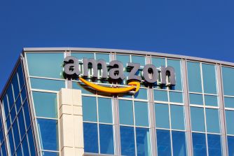 Amazon logo on a glass-front office building under a clear blue sky.