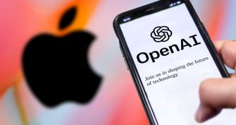 Apple logo in the background with a hand holding a smartphone displaying the OpenAI logo on the screen.