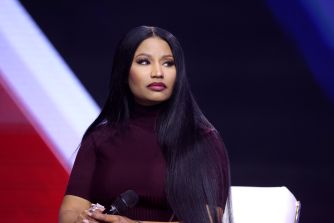 A woman with long black hair wearing a burgundy top stands on a stage.