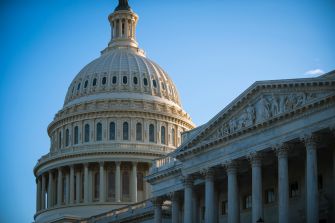 The U.S. Capitol dome and neoclassical façade against a clear blue sky.