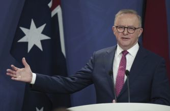 Man in a suit giving a speech at a podium with the Australian flag visible in the background.