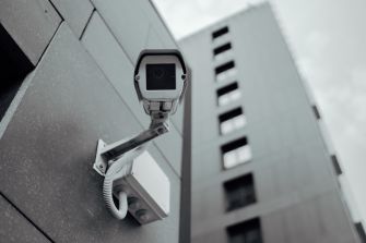 Close-up of a surveillance camera mounted on the outside of a tall building.
