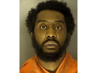 Mugshot of a man with a full beard wearing an orange prison jumpsuit.