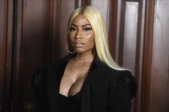 Portrait of a woman with long platinum blonde hair wearing a black blazer and low-cut top, posing indoors.