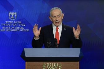 Man at a podium delivering a speech, with a blue backdrop featuring an official insignia.