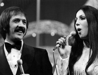 Black-and-white photo of a man and a woman performing on stage, each holding a microphone and dressed in formal attire.