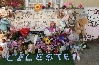 Memorial display outside a residence with flowers, candles, and stuffed animals, and a banner reading "Justice for ..." honoring the victim.