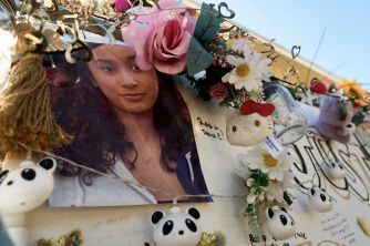 Memorial display with a large photo of a woman, surrounded by pink flowers, daisies, and panda plush toys.