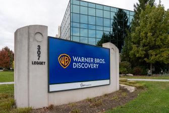 Warner Bros. Discovery sign on a grassy plaza with a modern glass building in the background.