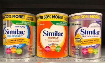 Three cans of Similac infant formula on a grocery store shelf.