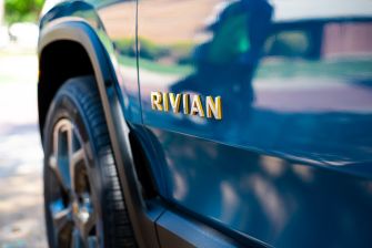 Close-up of a blue Rivian vehicle with a gold RIVIAN emblem on the side.