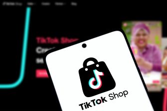 A tilted smartphone screen displays the TikTok logo and “TikTok Shop” branding, with a blurred livestream interface visible in the dark background.