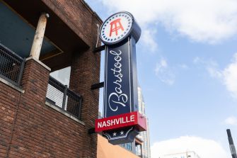 Barstool Sports sign mounted on a brick building in Nashville, featuring a vertical Barstool sign with a circular logo at the top and a red Nashville banner.