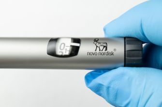 Blue-gloved hand holding a Novo Nordisk injection pen with the dose dial visible and the Novo Nordisk logo.