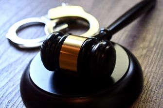 Gavel rests on a wooden surface with a pair of handcuffs in the background, symbolizing legal proceedings.