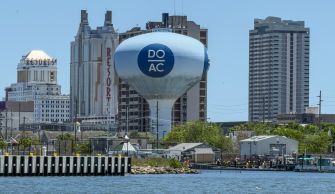 A blue-and-white Atlantic City water tower with a circular emblem rises above a harbor lined with high-rise hotels along the waterfront.