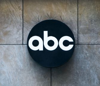 Circular black sign bearing the white lowercase "abc" logo mounted on a gray tiled wall.