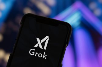 Smartphone screen displaying the Grok logo, held in front of a colorful, blurred background.