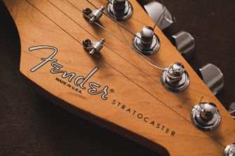 Close-up of a Fender Stratocaster headstock showing tuning pegs, the Fender logo, and the word Stratocaster on the wood.