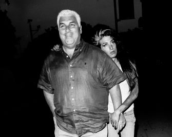 A man in a short-sleeve shirt walks with a woman who has long hair, together outdoors at night.