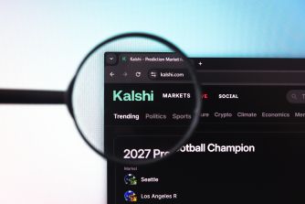 Close-up of a laptop screen showing the Kalshi prediction market site, with a magnifying glass highlighting the Kalshi page.