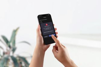 Close-up of hands holding a smartphone displaying a red warning alert on the screen.