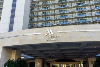 Entrance to the Anaheim Marriott hotel with the Marriott logo above the porte-cochère; a high-rise building with curved balconies forms the background.
