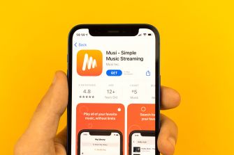 A hand holds a smartphone displaying the Musi app listing in an app store, set against a bright yellow background.