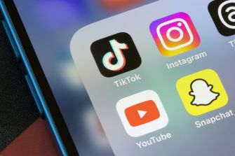 Close-up of a smartphone screen displaying social media app icons for TikTok, Instagram, YouTube, and Snapchat.